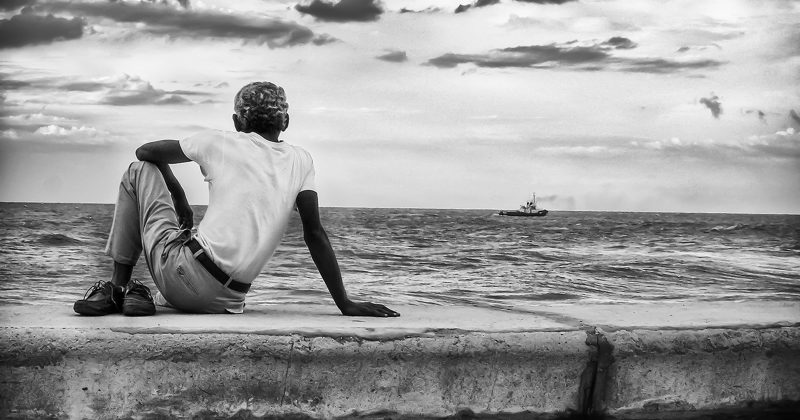 Black and white photograph of a man sitting on Havana's seawall