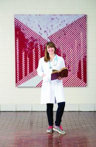 Natalie Deuitch is interested in pursuing a career in public health. She stands in front of the painting 'Warning Sign' by Allison Tierney (MFA '15) in the Hanes Art Center. (photo by Steve Exum)