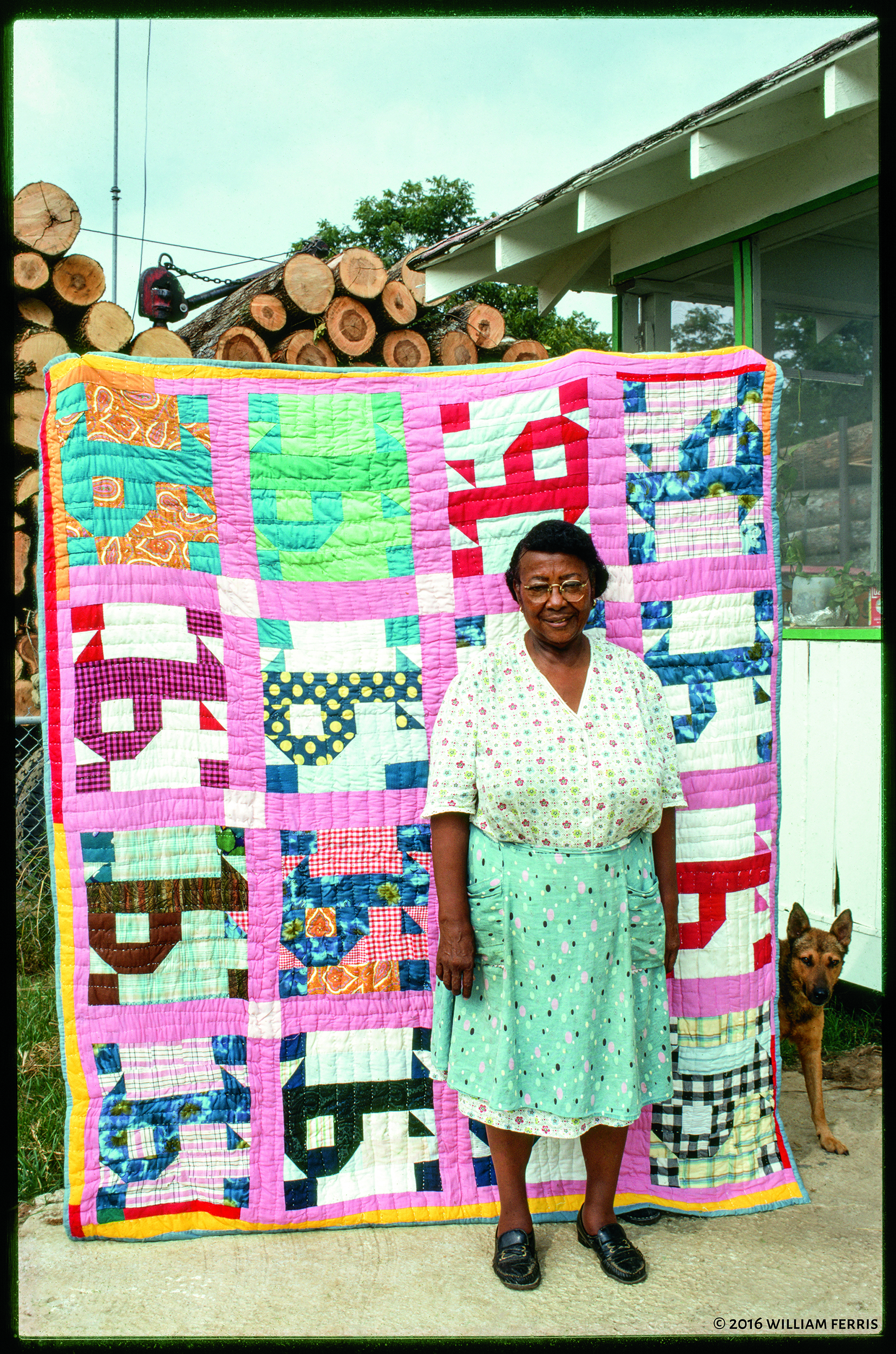 Pecolia Warner stands in front of a colorful quilt decorated with squares with 'P' in them