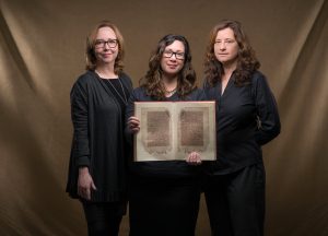Jan Chambers, Glaire Anderson and Laura Miller hold a facsimile of an 11th-century Arabic manuscript