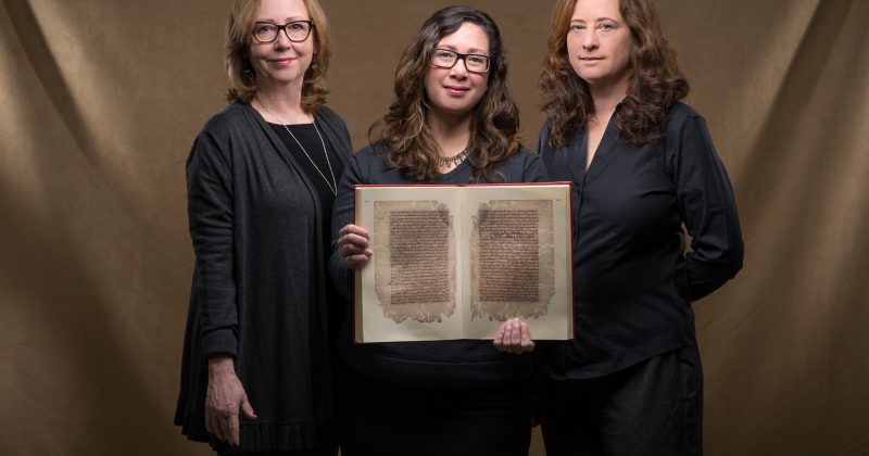 Jan Chambers, Glaire Anderson and Laura Miller hold a facsimile of an 11th-century Arabic manuscript