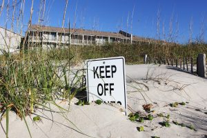 A sign buried in sand: "KEEP OFF..." The final line is covered in sand.