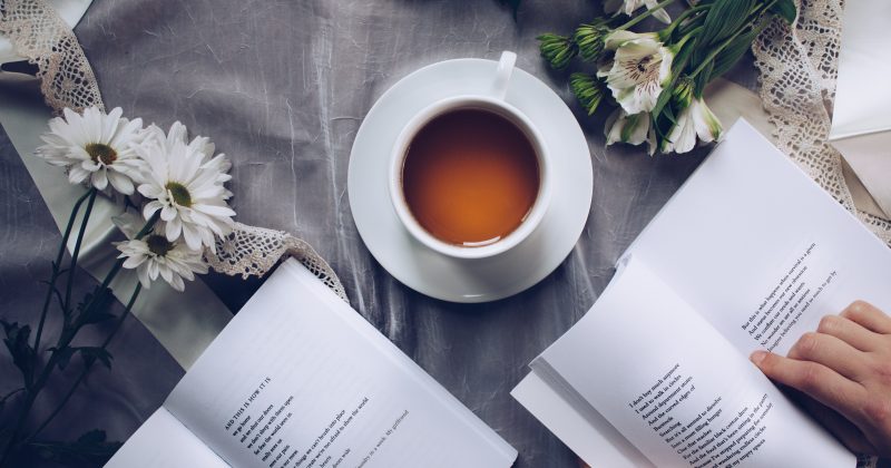 photo of open books with a cup of coffee on a table and flowers surrounding the books and coffee