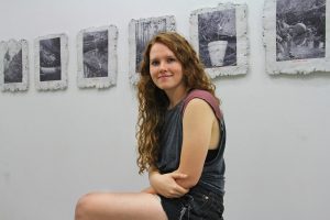 Meredith Emery sits in the Art Lab, behind her are stone slabs with her photographs pasted on top.
