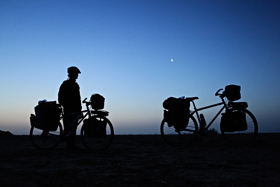 Photo at night -- silhouettes -- of Kate Harris and Mel Yule with their bikes -- against a starry sky.