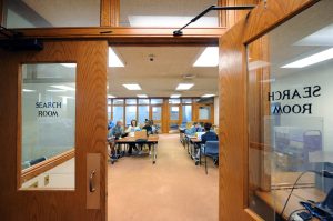 Students pored over letters and financial documents in Wilson Library. Photo shows wide room with students at a table and the words "reading room" on the doors of the Wilson Library space.