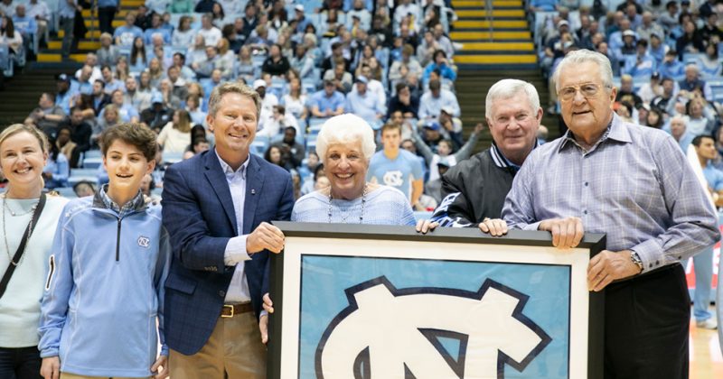 Kevin Guskiewicz presents Billie and Donn Stallings and family with a large UNC frame at a basketball game.