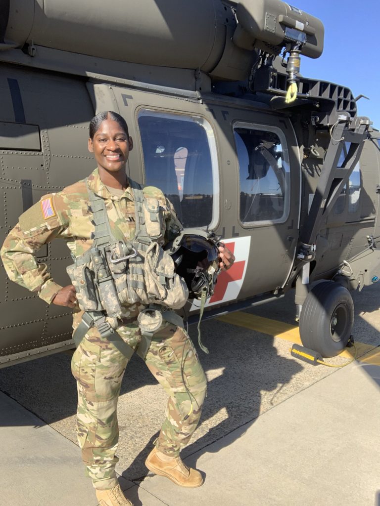 Lindsey Jefferies in uniform, smiles in front of a Black Hawk medical helicopter.