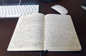 Notes written across two pages from Oswaldo Estrada's journal, on his desk next to a computer laptop and mouse.