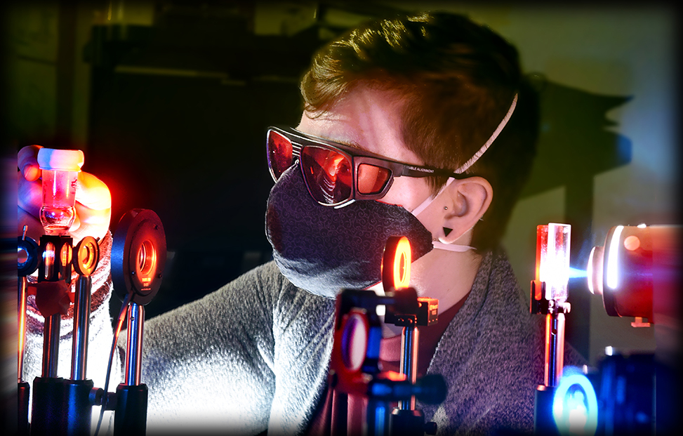 Rachel Bangle works in the laser lab with a mask on and pulsing lights around her.