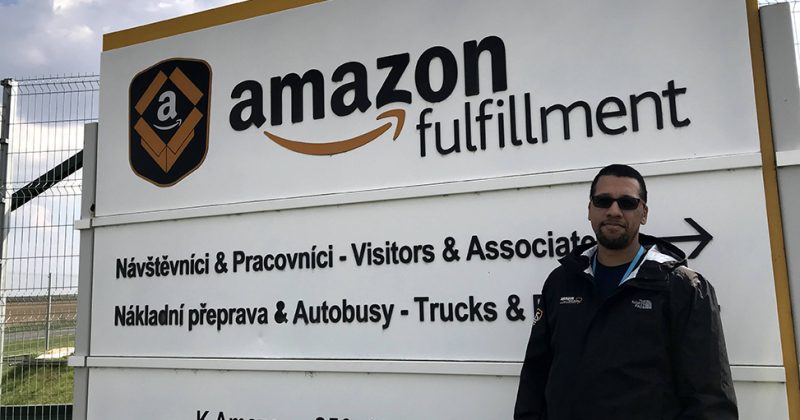 Hakeem Smith pictured standing outside of an Amazon fulfillment site with the sign reading in Czech foreign language