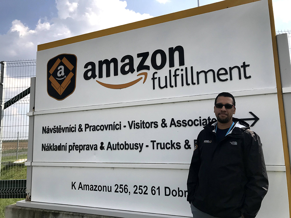Hakeem Smith pictured standing outside of an Amazon fulfillment site with the sign reading in Czech foreign language