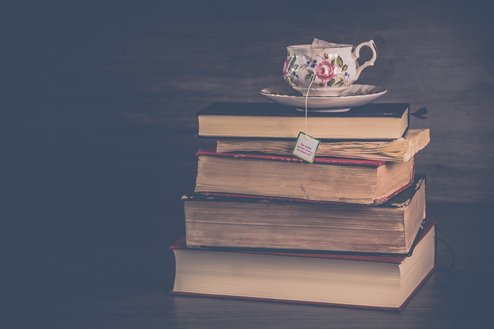 Stack of books on a dark black background with a coffee or tea mug sitting on top.