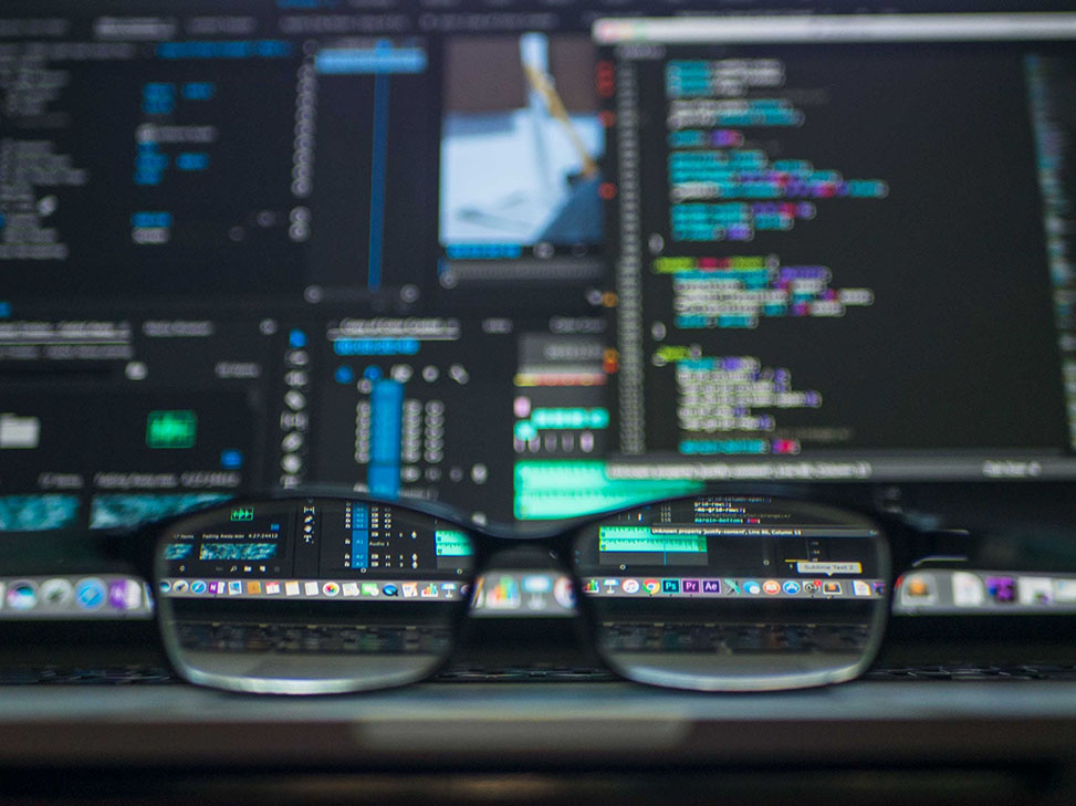 A picture of eye glasses sitting on a laptop screen filled with code