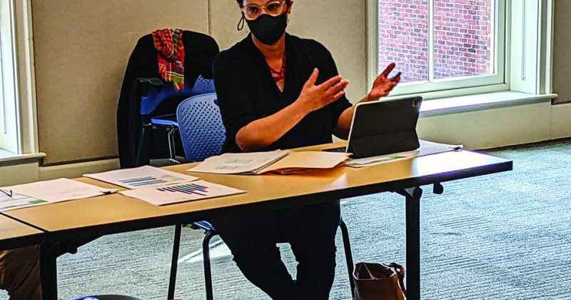 Karla Slocum with a mask on sitting at a table speaking