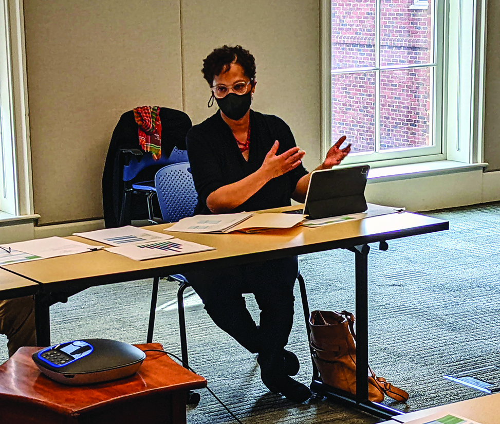Karla Slocum with a mask on sitting at a table speaking