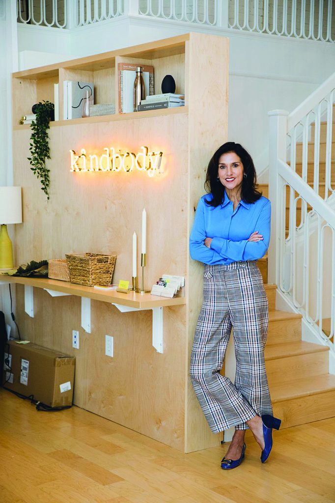 Gina Bartasi leans in front of wall bearing the name of her fertility care facility, Kindbody