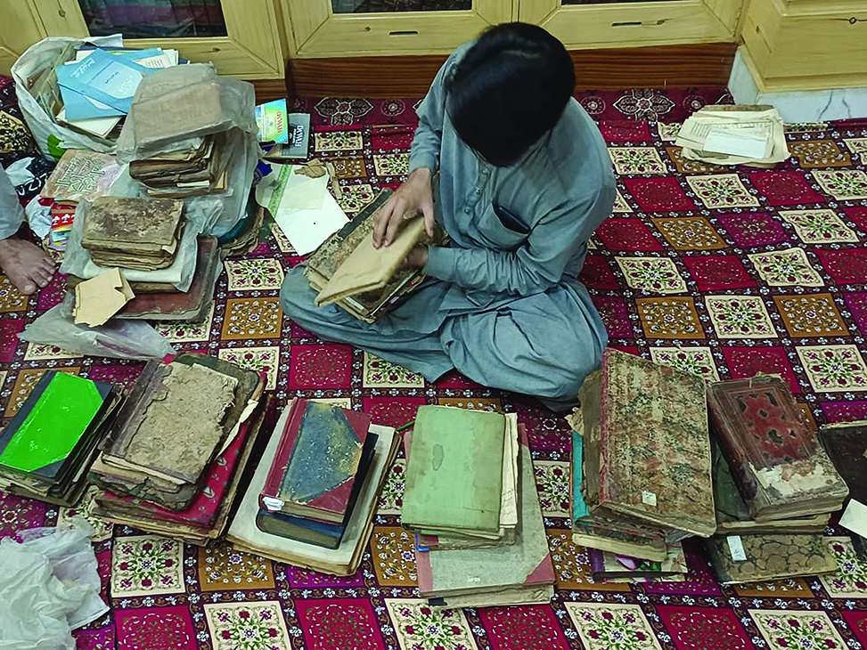 A man sits on the ground examining rare manuscripts.