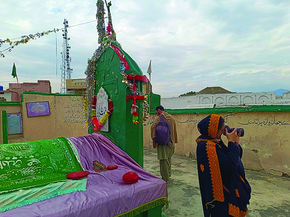 A woman on a rooftop takes photos from an ancient shrine in Thana, Malakand.
