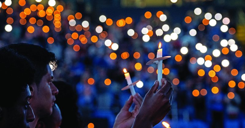 People hold candles in the darkness at a memorial tribute to Zijie Yan in the Dean E. Smith Center.