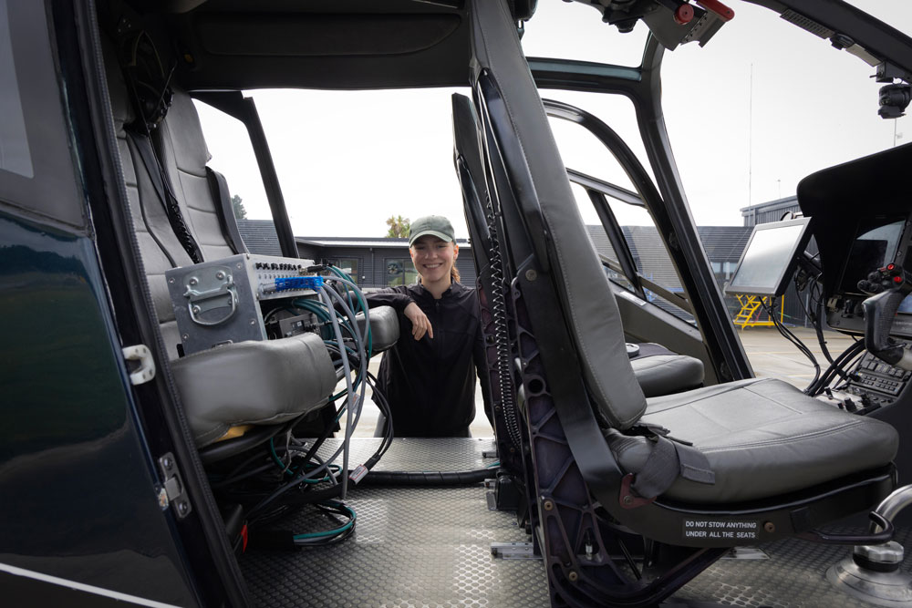 The interior of a helicopter, Marissa Dudek standing at the far side and looking through the helicopter at the camera.