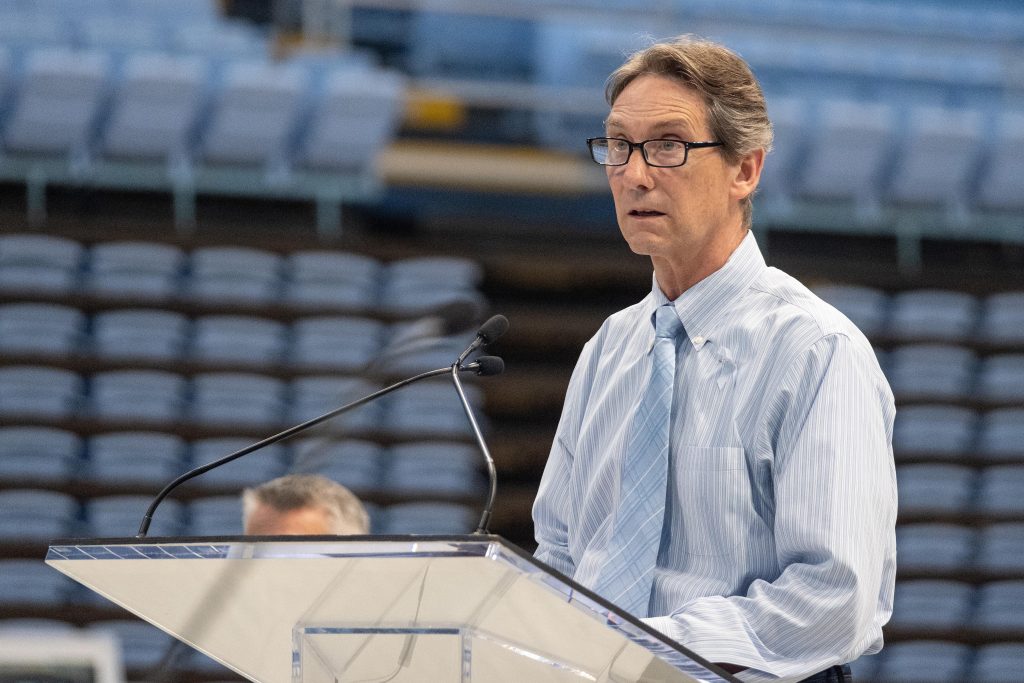 Dean White stands at a podium and speaks at the Dean E. Smith Center.
