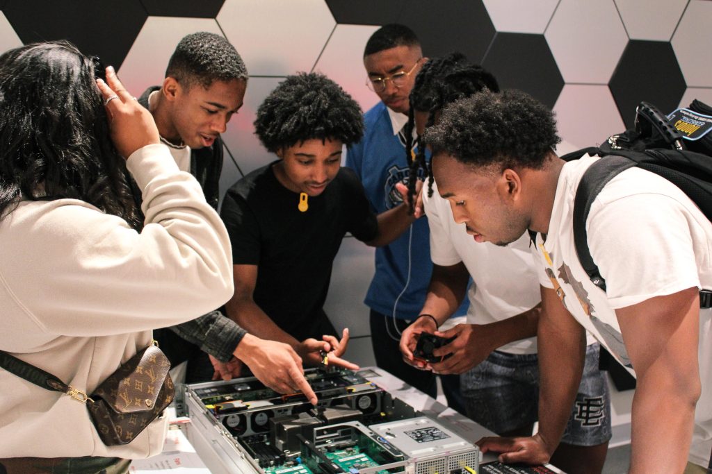 Five students gather around  an exhibit that features computer components.