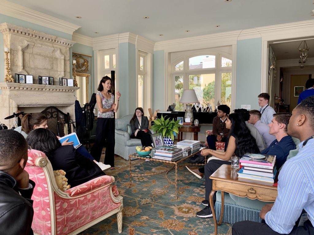 Students sit on couches and chairs around a living room as they listen to a lecture in the home of UNC alumna Robin Richards Donohoe.