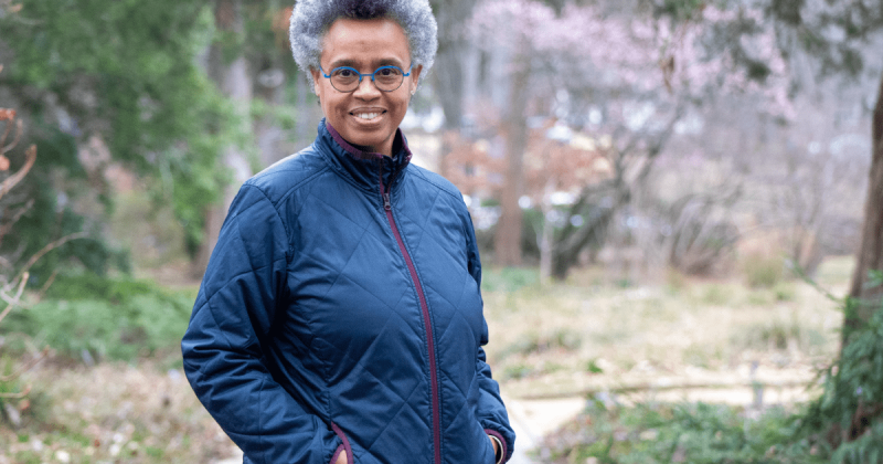 Annette Lawrence has her hands in her pockets in the arboretum on UNC