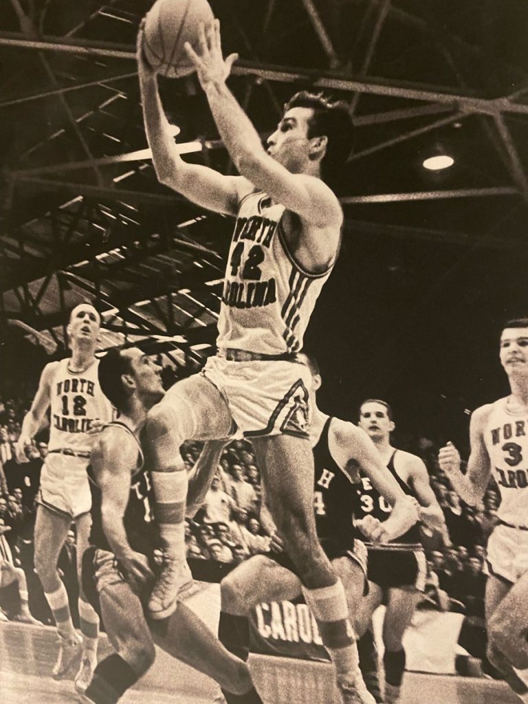 Black-and-white archive picture of a young Charles Shaffer mid-air, holding a basketball, during a UNC basketball game.