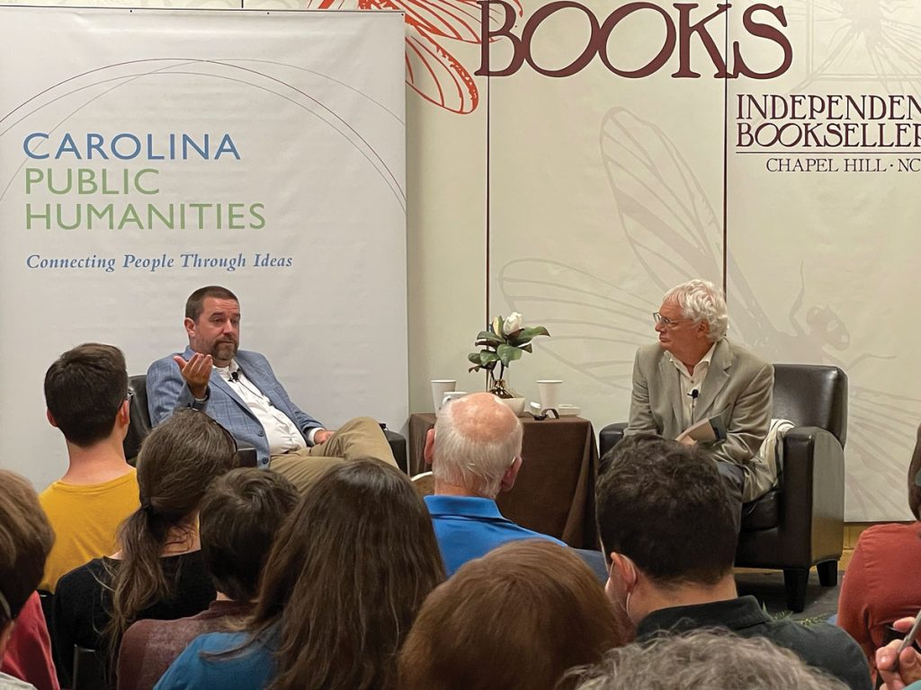 Mike Duncan (left) and Lloyd Kramer have a discussion in front of a crowd. Behind them are banners announcing "Carolina Public Humanities" and "Flyleaf Books." 