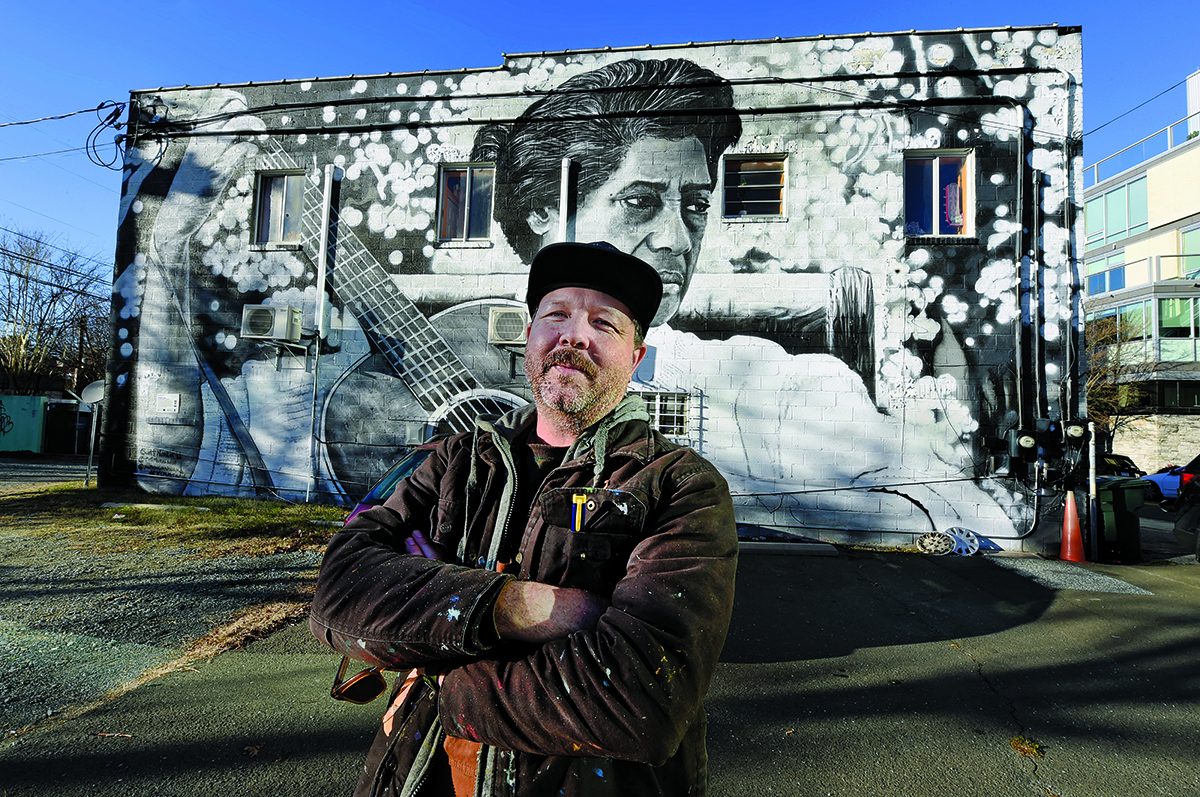 Scott Nurkin stands, arms crossed, in front of the Elizabeth Cotten mural.