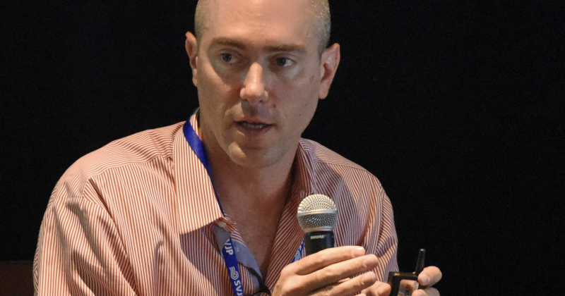 David Rosenberg speaks into a microphone on stage during a conference
